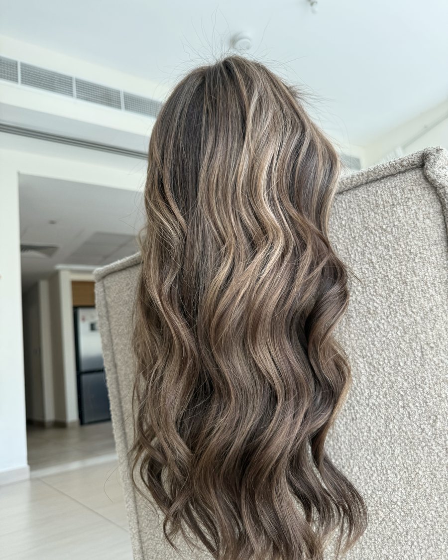 Long hair seen from behind, light brown with cool blonde highlights, styled in deep waves to the mid-back.