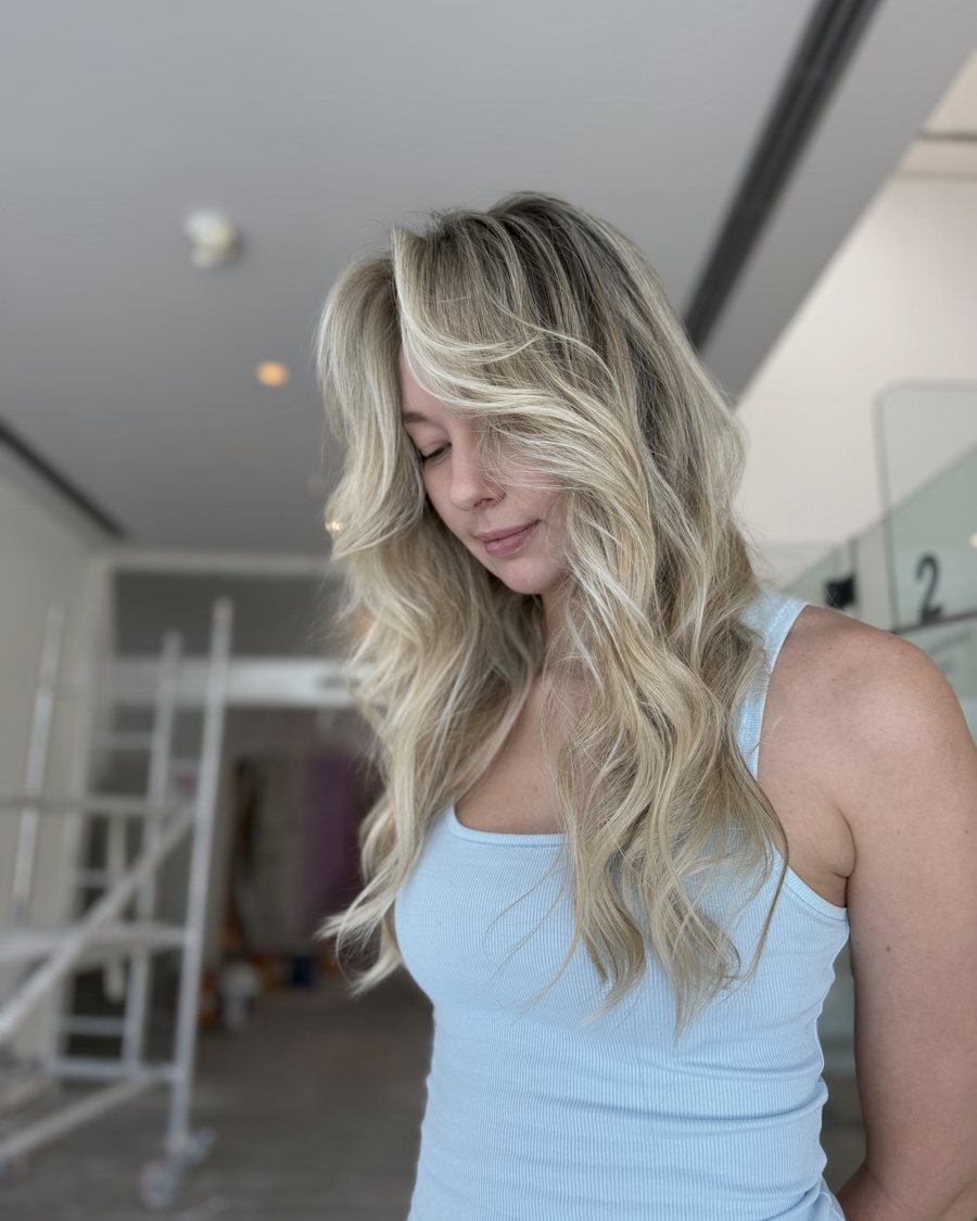 Long blonde hair with a darker root and face-framing layers, styled in loose waves.